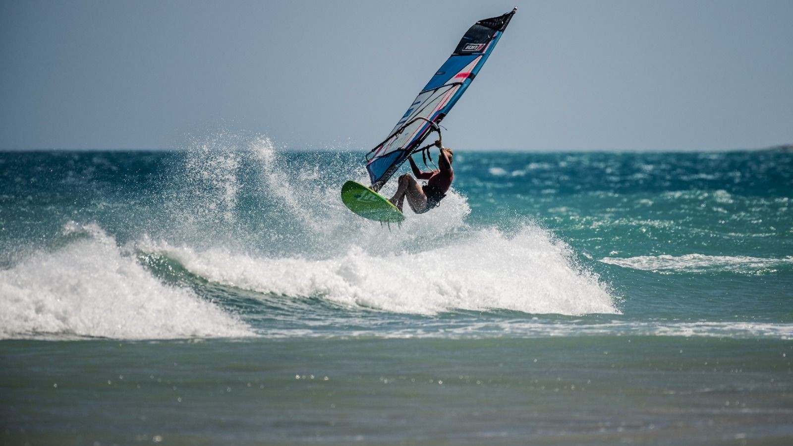 Windsurfer catching air over a wave in the ocean on a clear day.