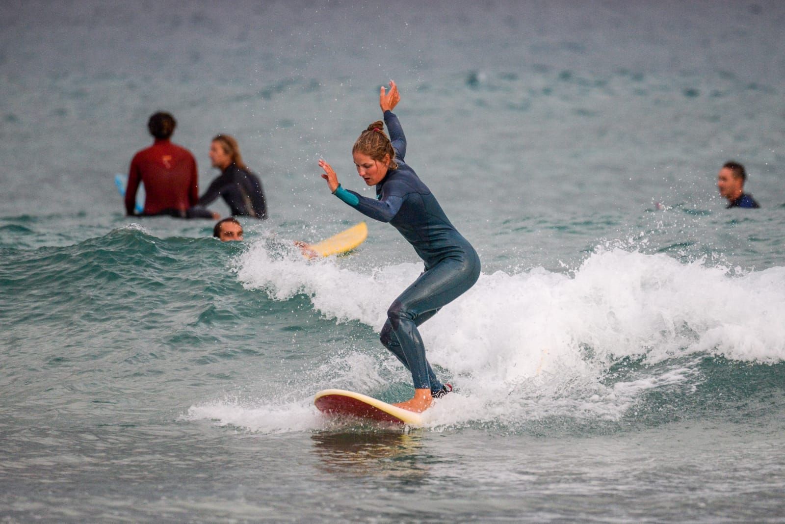 Person in a wetsuit surfing on a small wave with three other surfers in the background.