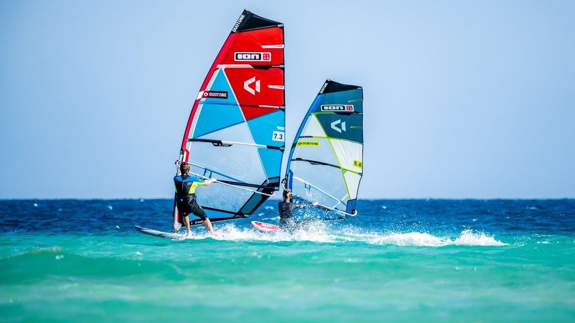 Two windsurfers riding waves with colorful sails on a sunny day.